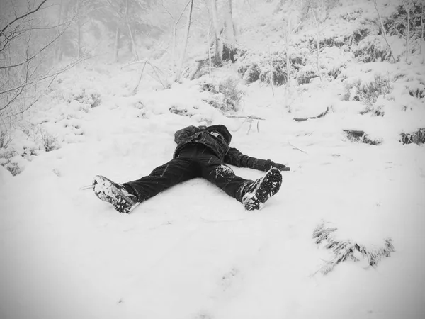 Ragazzo divertente sdraiato in cumulo di neve. Bambino gioco nella neve fresca sulla collina sassosa — Foto Stock