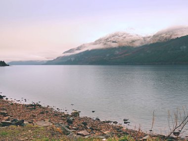 Karlı dağ ve göl, Bahar yatay. Alçak bulutlar 