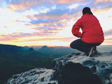 Kayaya oturan uzun yürüyüşe çıkan kimse. Kırmızı siyah sıcak giysiler erkekte cliff üzerinde oturan ve uzak manzarayı. 