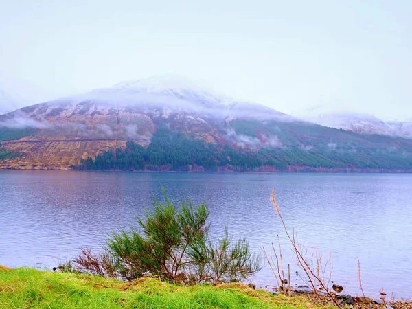 Jarní krajina s zasněžené hory a jezero. Nízká oblačnost — Stock fotografie