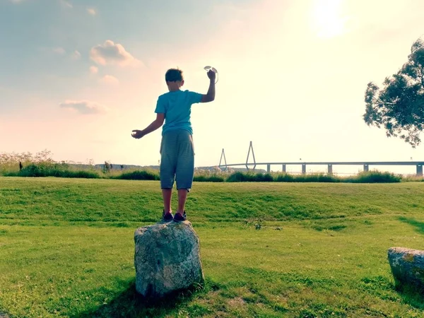 El chico rubio está jugando en el lado del mar. Gran puente de tráfico entre islas en el horizonte . — Foto de Stock