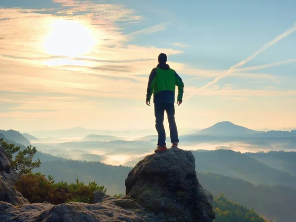 Homem ficar no pico rochoso dentro do amanhecer e olhar sobre a paisagem enevoada . — Fotografia de Stock