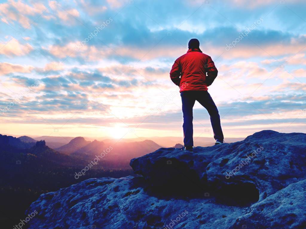 The figure of the men in red jacket on sharp cliff. Mountains within early fall daybreak