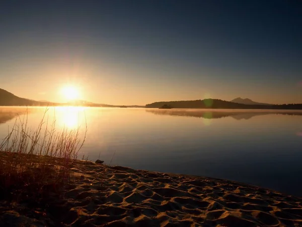 Verlassener Sandstrand am See, klarer Himmel vor Sonnenuntergang, Sonnenstrahlen am Horizont — Stockfoto