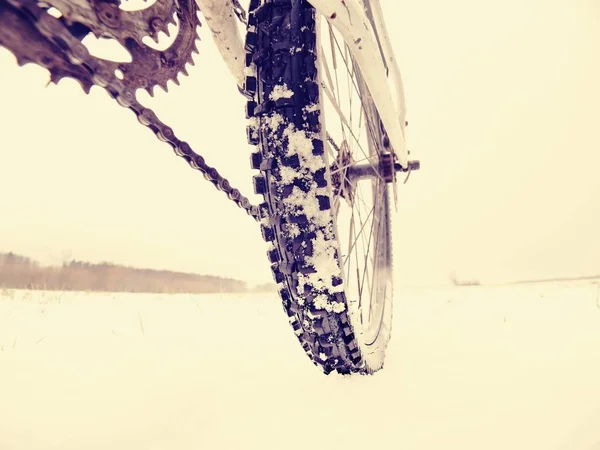 Rear wheel of mountain bicycle in snowy meadow in countryside. Detail of bike