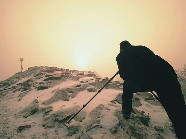 Fotógrafo com olho no visor da câmera no tripé ficar em precipício nevado e tira fotos . — Fotografia de Stock