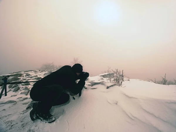 Fotografo sdraiato sulla neve sulla vetta della montagna e scatta una foto di paesaggio fantastico — Foto Stock