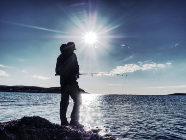 Genç bir gölde balıkçılık gün batımında adam. Bir olta ile yalnız adam kayalık kıyısında duruyor 