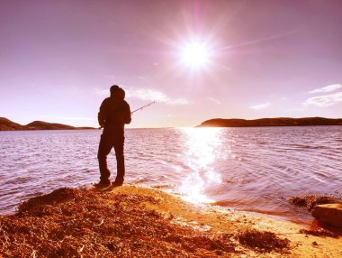 Genç bir gölde balıkçılık gün batımında adam. Bir olta ile yalnız adam kayalık kıyısında duruyor 