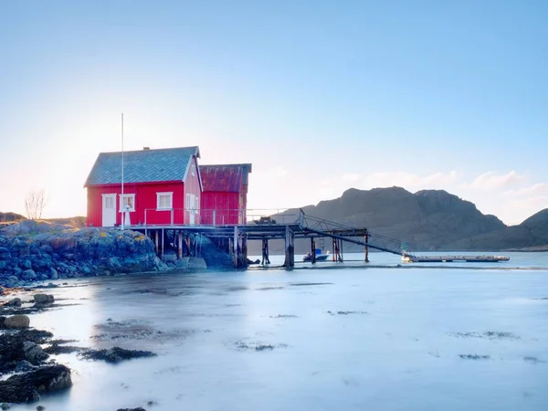 Norveç balıkçı köyü taşlık adada. Kırmızı beyaz evler sessiz Bay shinning. Yumuşak su seviyesi yansıtma — Stok fotoğraf