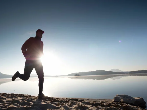 Silhueta de corredor atlético correndo na praia contra o nascer do sol . — Fotografia de Stock