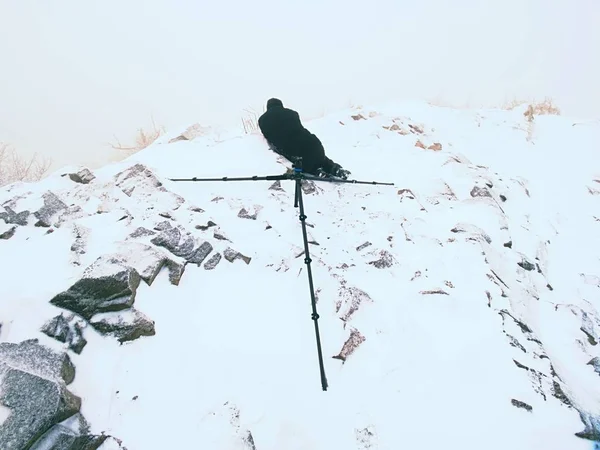 Fotógrafo colocar na neve e tirar foto de grama congelada com câmera de espelho no pescoço . — Fotografia de Stock