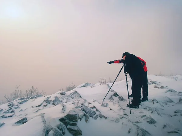 Wanderer und Foto-Enthusiasten bleiben auf verschneiten Gipfeln am Stativ stehen. Männer auf Klippen sprechen und denken. — Stockfoto