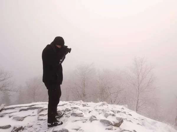 Путешествующий фотограф делает фотографии в древних камнях на снежной вершине горы. Зимнее утро — стоковое фото