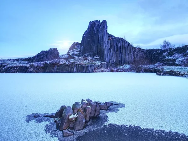 Peak of basalt pillars covered by snow, frozen pool. Full moon in blue sky in the background. — Stock Photo, Image