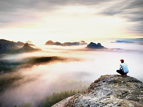 Young hiker in white and black siuts  on cliff edge looking to misty hilly valley bellow, fall begins — Stock Photo, Image