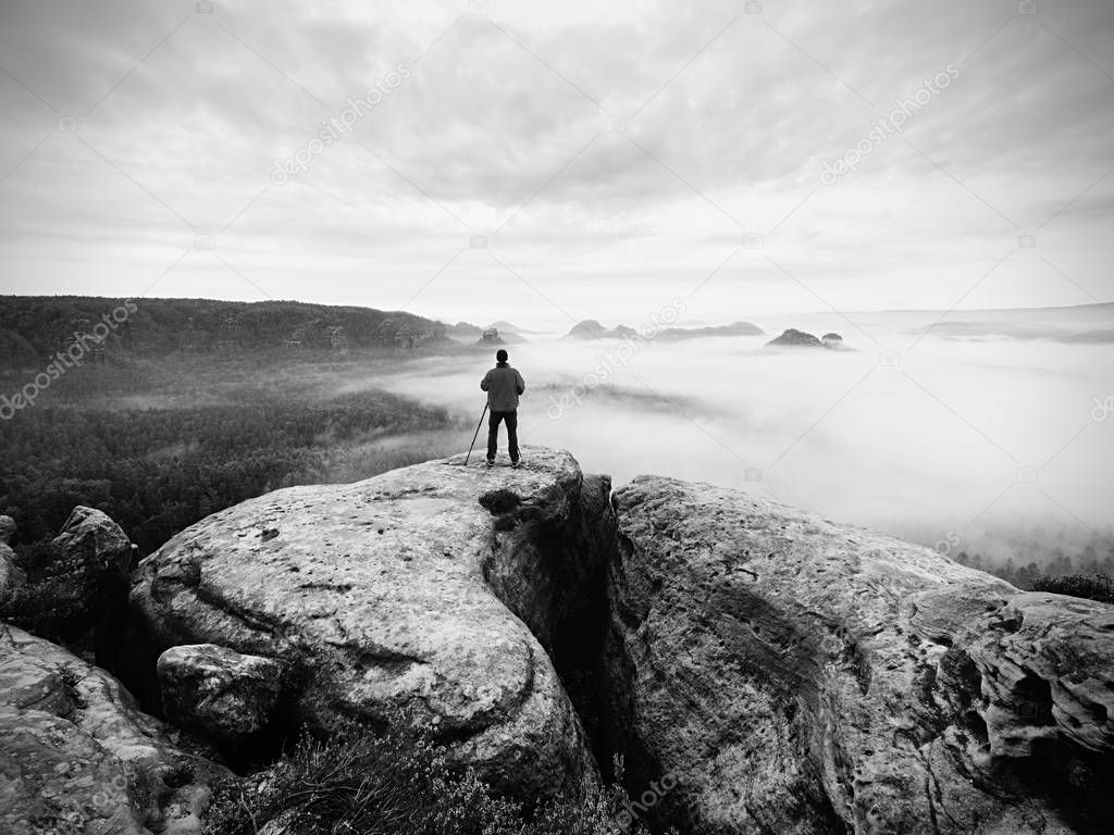 Artist photographer works with tripod on cliff above clouds. Dreamy fogy landscape,
