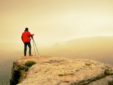 Sanat fotoğrafçısı yere tepe kaya üzerinde kamera ile fotoğraf çeker. Sisli manzara