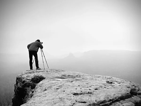 Профессиональный фотограф фотографирует туманный пейзаж с зеркальной камерой и штативом . — стоковое фото