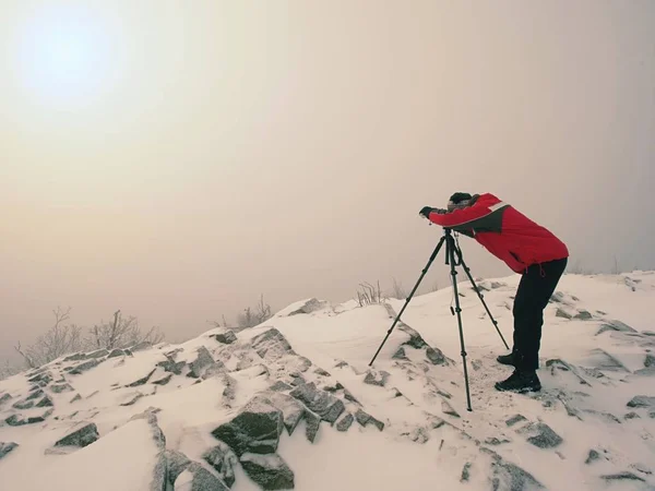 Путешествующий фотограф делает фотографии в древних камнях на снежной вершине горы. Зимнее утро — стоковое фото