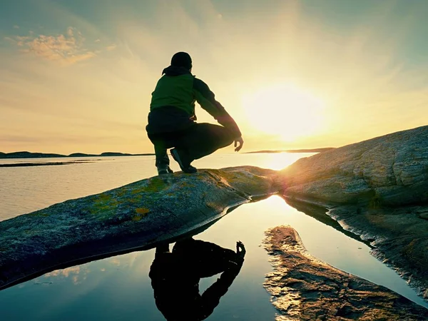 Один турист сидить на скелястому березі і думає. Розслабляючись на красивому багатобарвному заході сонця — стокове фото