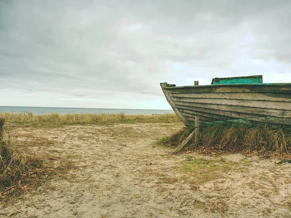 Zertrümmertes Fischerboot auf altem trockenen Gras. Verlassenes Holzschiff mit beschädigtem Motor — Stockfoto