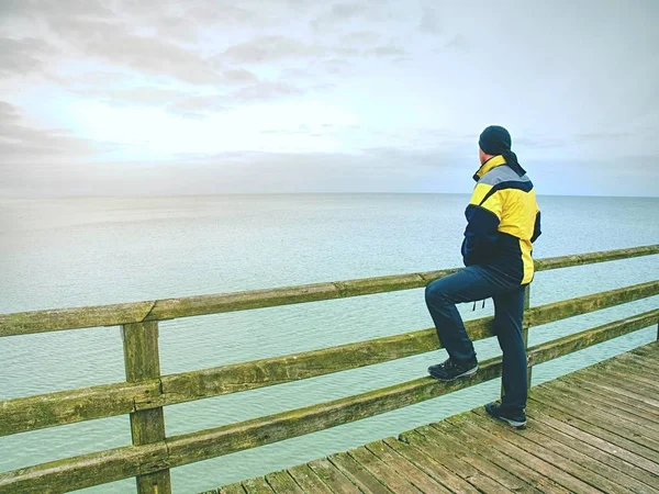 Man thinking. Tourist  in warm clothes on sea mole at handrail. Tourist on pier in harbor — Stock Photo, Image