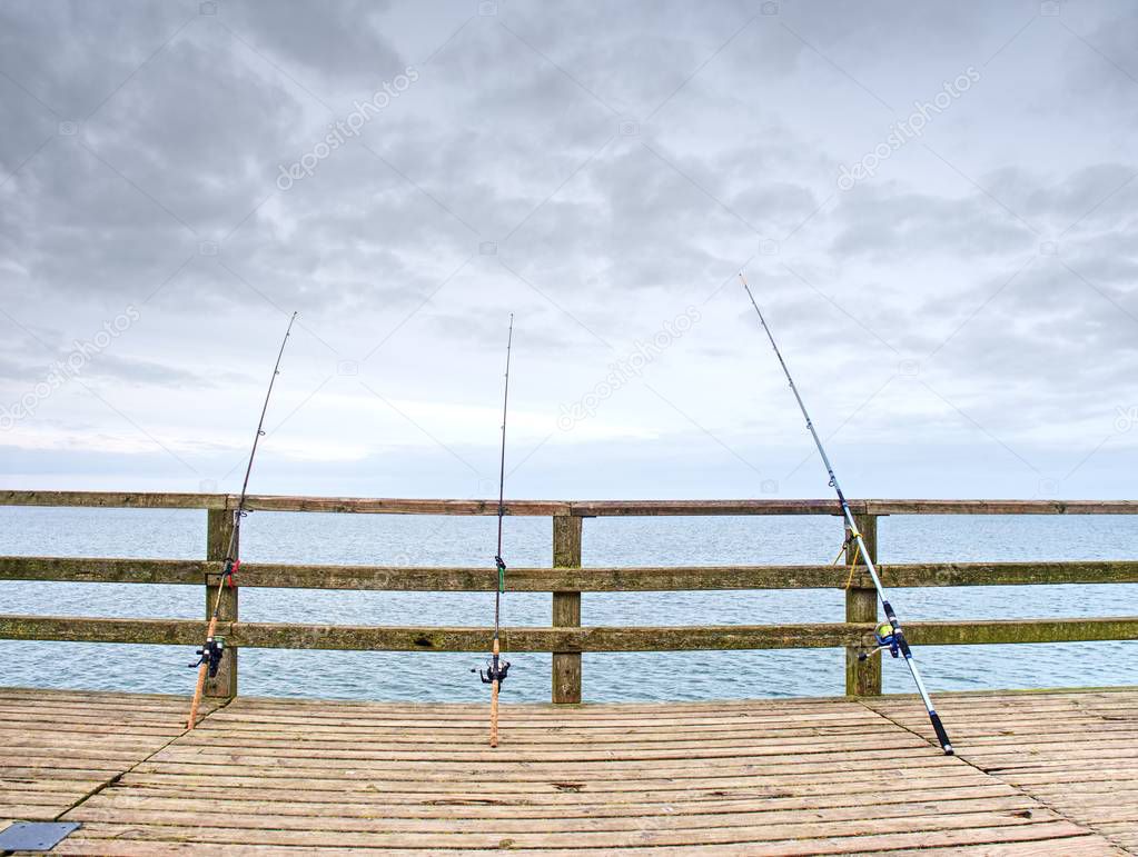 Several fishing rods against the wooden railing of the beach pier. 