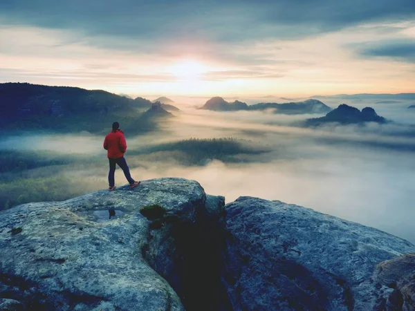 Hiker in red jacket enjoy view over clouds. Mountain rocky peak — Stock Photo, Image