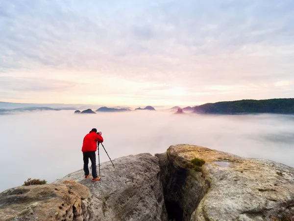 Professioneller Fotograf über Wolken. Mann fotografiert mit Kamera auf Stativ auf felsigem Gipfel. — Stockfoto