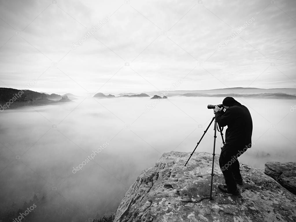 Artist photographer works with tripod on cliff above clouds. Dreamy fogy landscape,