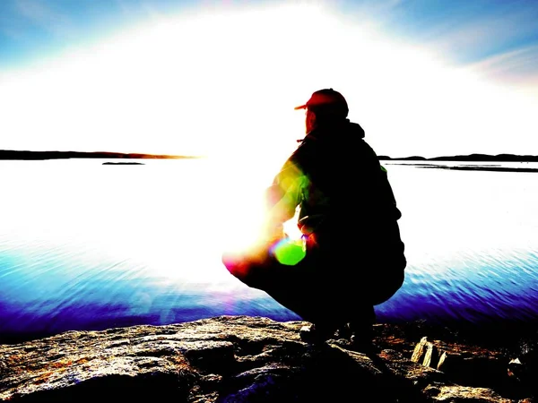 Einsamer Wanderer sitzt allein an der Küste und genießt den Sonnenuntergang. Blick über felsige Klippen zum Meer — Stockfoto