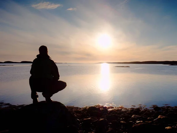 Solo turista sedersi su una riva rocciosa e pensare. Rilassarsi in un bellissimo tramonto multicolore — Foto Stock