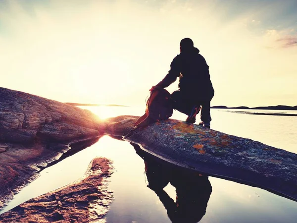 Jeune voyageur au coucher du soleil. Touriste assis sur la falaise au-dessus du lac — Photo