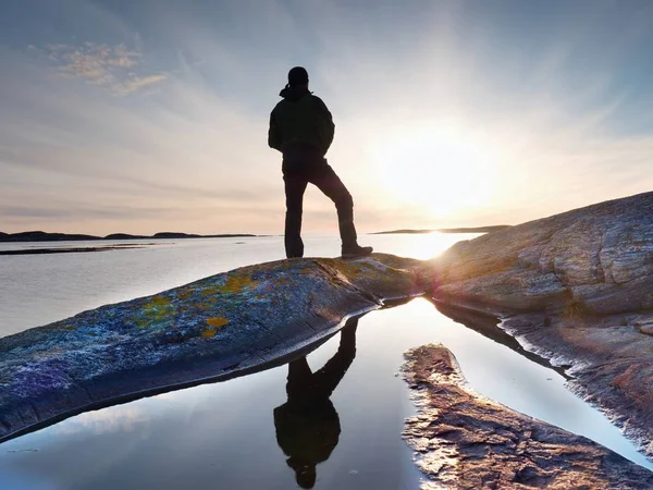 Joven hombre de pie con mochila. Caminante en la piedra en la orilla del mar en el cielo colorido del atardecer . — Foto de Stock