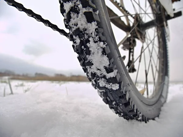 Dettaglio ruota posteriore di mtb. Fiocchi di neve si sciolgono su pneumatici scuri fuoristrada. Inverno in campo . — Foto Stock
