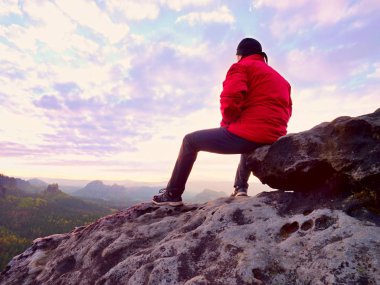 Kayaya oturan uzun yürüyüşe çıkan kimse. Kırmızı siyah sıcak giysiler erkekte cliff üzerinde oturan ve uzak manzarayı. 
