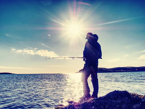 L'uomo attivo sta pescando in mare dalla costa rocciosa. Pescatore controllo spingendo esca — Foto Stock