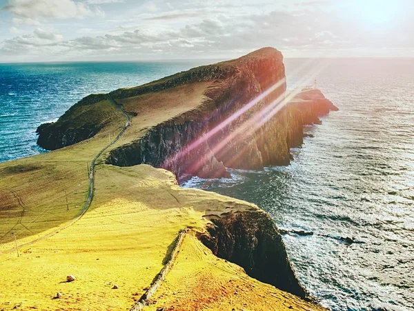 Neist Point lighthouse på stenig klippa ovanför vågiga havet. Blå kväll havet och vassa klippor, — Stockfoto