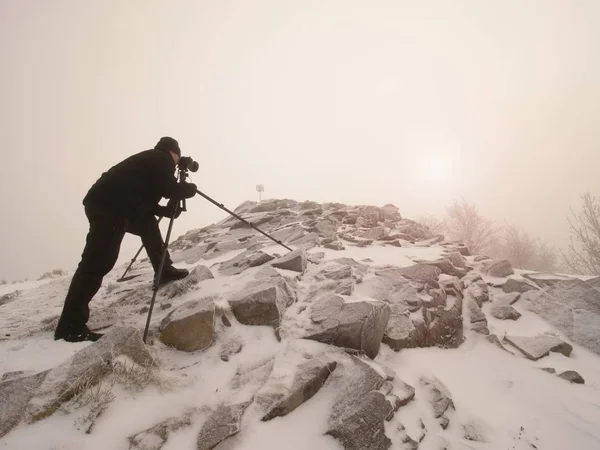 Fotógrafo de viajes haciendo fotos en piedras antiguas en el pico nevado de la montaña. Mañana de invierno —  Fotos de Stock