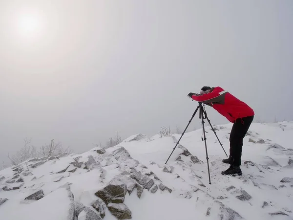 Muž si focení v bouřlivé zimní přírodě. Fotograf přírody při pohledu do hledáčku — Stock fotografie