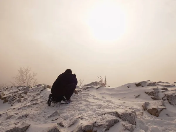 Professional photographer lay down to snow and takes photos with mirror camera on peak