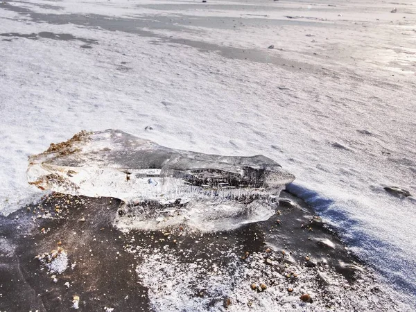 Blue ice of frozen sea and small ice fragments. Hilly island at far horizon.