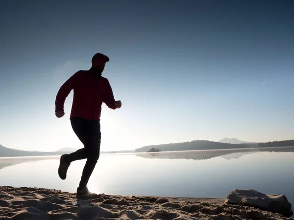 Running man to beautiful sunset on tropical white sand beach under blue sky. Beach sports