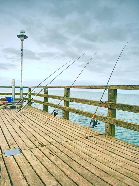Πολλά καλάμια ψαρέματος κατά τα ξύλινα κάγκελα από την προβλήτα παραλίας. — Φωτογραφία Αρχείου