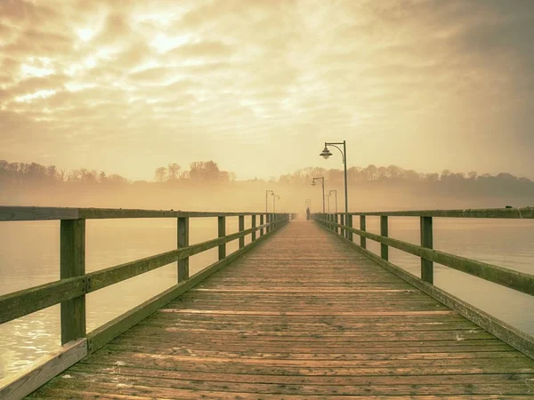 Tomma trä piren i hamnen. Stål lyktstolpe, Horisont gömd i tjock dimma. Hösten mist — Stockfoto