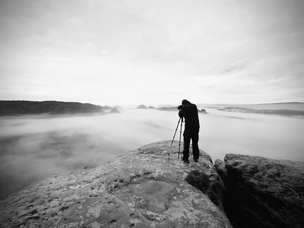 Künstler Fotograf arbeitet mit Stativ auf Klippe über Wolken. verträumte Nebellandschaft, — Stockfoto