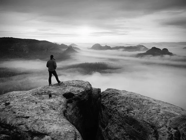 Randonneur sur le pic rocheux. Merveilleux lever du jour dans les montagnes, brouillard épais dans la vallée profonde. . Photo noir et blanc . — Photo