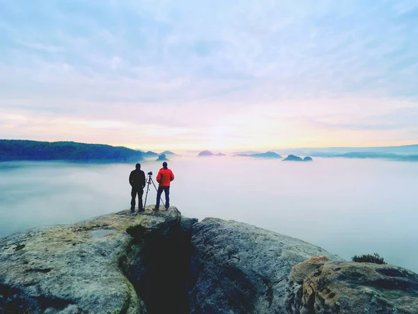 Dois fotógrafos de casaco quente com tripé atirar fotos de paisagem outonal abaixo da montanha . — Fotografia de Stock