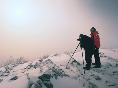 Uzun yürüyüşe çıkan kimse ve fotoğraf meraklısı tripod, karlı tepe üzerinde kal. Konuşma ve düşünme cliff adam.